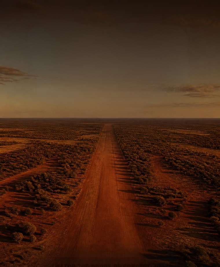 A straight red dirt road running to the horizon through open scrub at last light